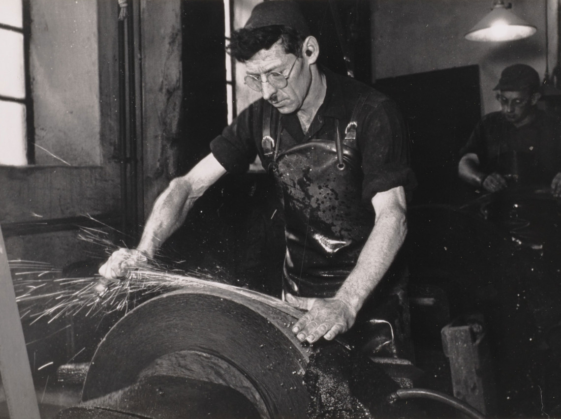 A scythe smith sharpening a scythe. Black-and-white photo from the 1950s.