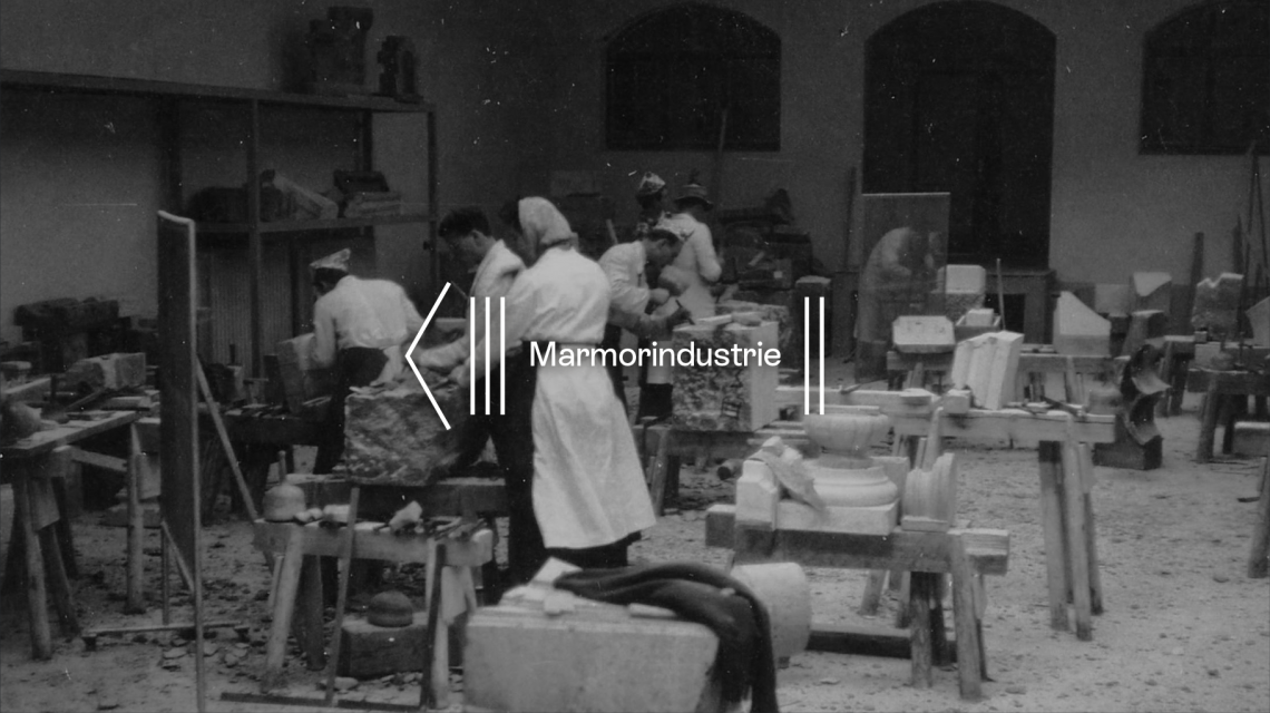 Black-and-white photo of marble workers shaping stone inside a traditional workshop hall.
