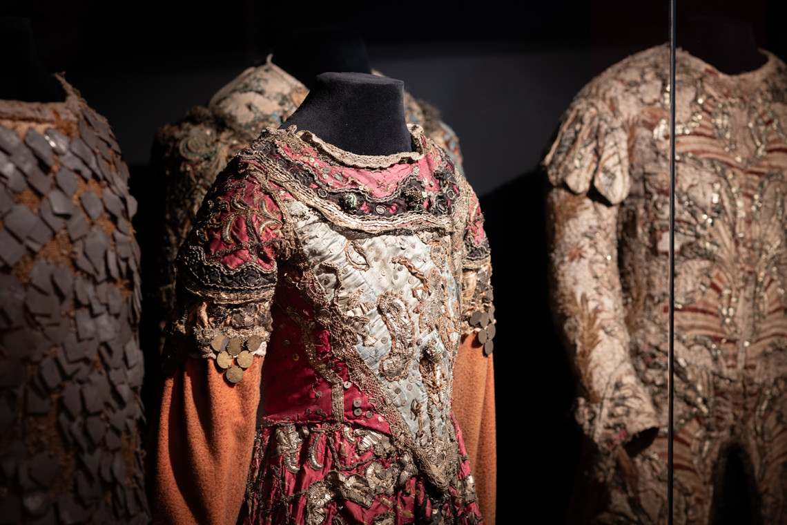 Close-up of the vitrine containing precious historical theatre costumes in shades of red and copper with metal embroidery.