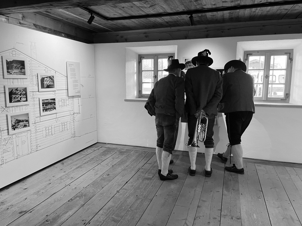 Three people wearing traditional costumes stand hunched over an exhibit in the house history room
